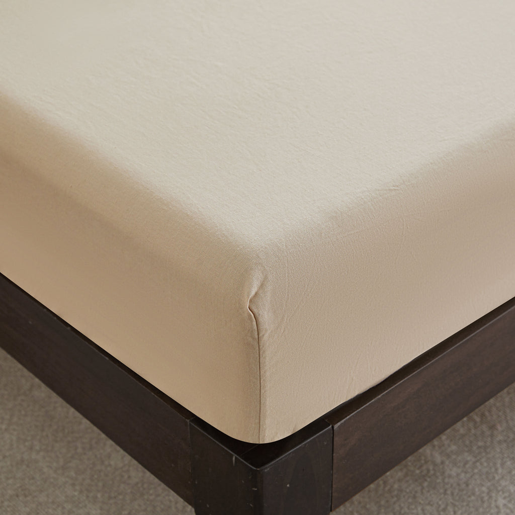 Beige fitted sheet on a bed with a wooden frame.